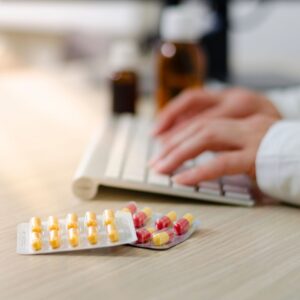 person typing on computer next to medication